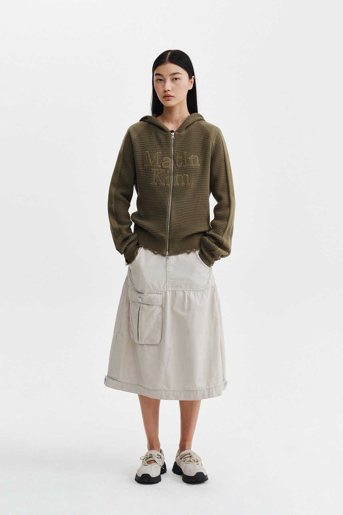 Áo sơ mi unisex màu khaki có mũ trùm, khóa kéo giữa trước, tay dài và logo Matin Kim