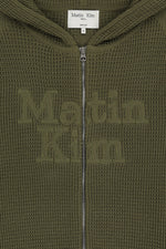 Áo sơ mi unisex màu khaki có mũ trùm, khóa kéo giữa trước, tay dài và logo Matin Kim