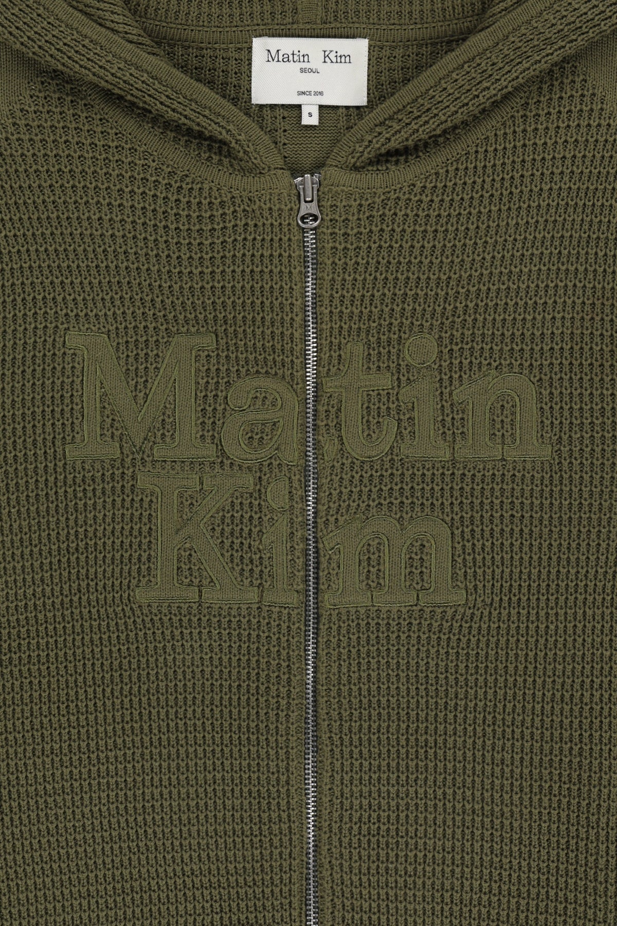 Áo sơ mi unisex màu khaki có mũ trùm, khóa kéo giữa trước, tay dài và logo Matin Kim