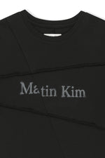 Áo top unisex với đường cắt chéo và logo Matin Kim, phom hộp màu đen.