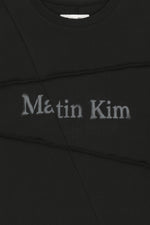 Áo top unisex với đường cắt chéo và logo Matin Kim, phom hộp màu đen.